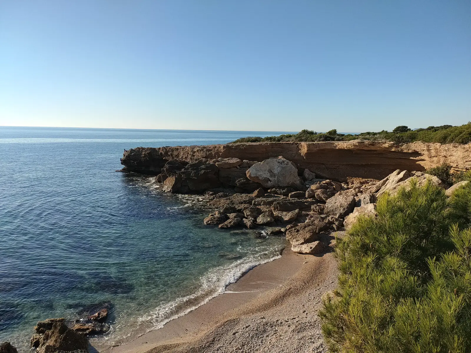 Pequeña cala de arena al pie de las rocas en la costa de la Sierra de Irta