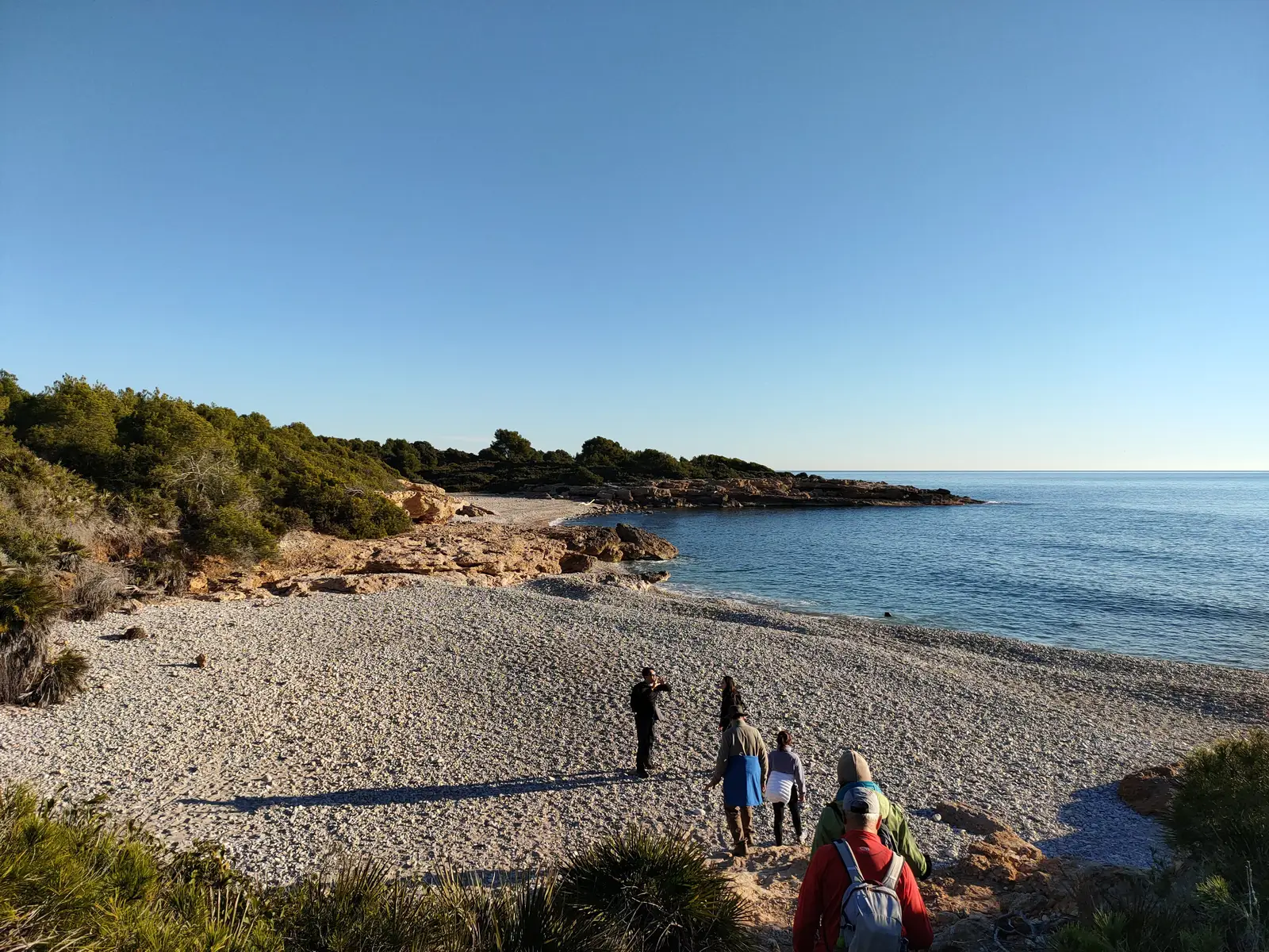 Senderistas en una cala de cantos rodados de la Sierra de Irta, entre pinos